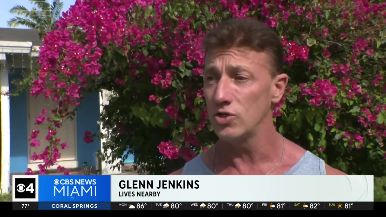 A close-up shot of Glenn Jenkins, a local resident, speaking during an interview with a background of vibrant pink bougainvillea flowers.
