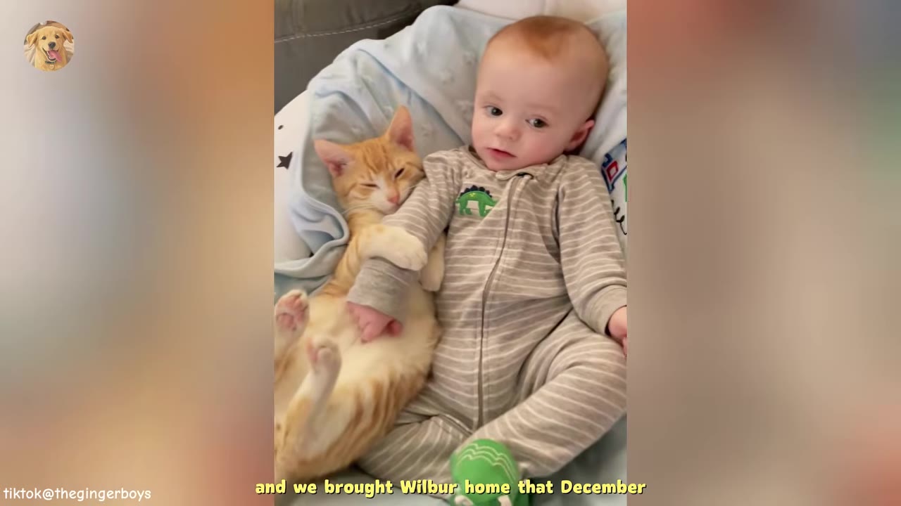 An orange tabby kitten cuddles next to a baby wearing striped pajamas, holding onto the baby's arm.