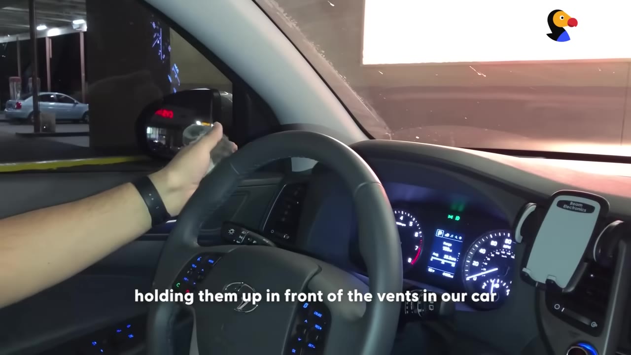 A close-up shot from inside a car showing a person's hand on the steering wheel while driving at night.