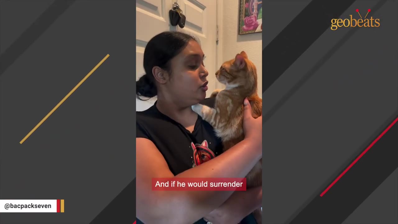 A woman with dark hair tied back holds an orange and white cat in her arms, looking at it closely as she speaks.