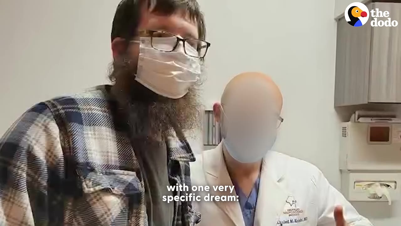 A bearded man wearing glasses and a surgical face mask stands next to a medical professional in a white lab coat inside a hospital setting.