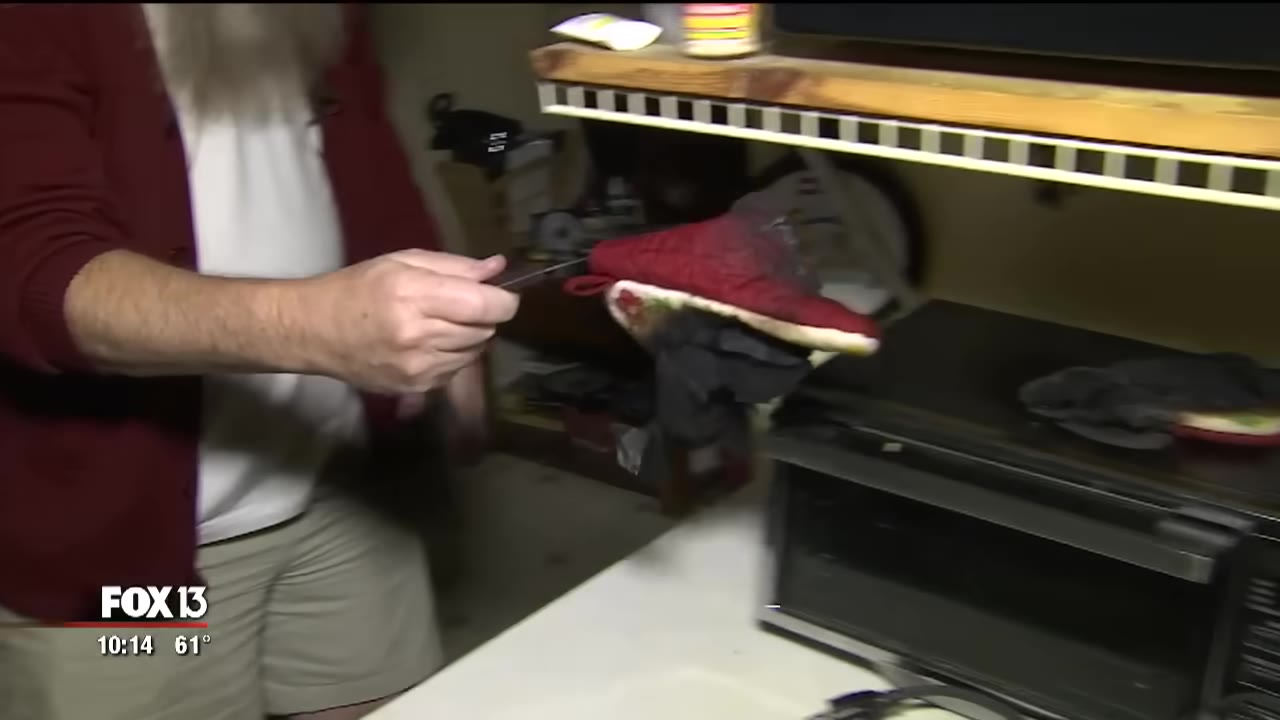 A man holds up a charred, burnt red oven mitt with a pair of tongs next to a toaster oven.