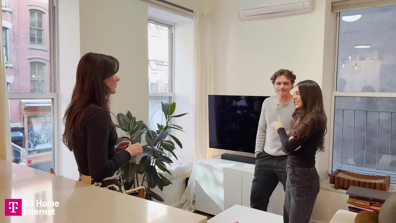 A man and a woman stand in their minimalist, modern apartment talking to a woman with long dark hair.