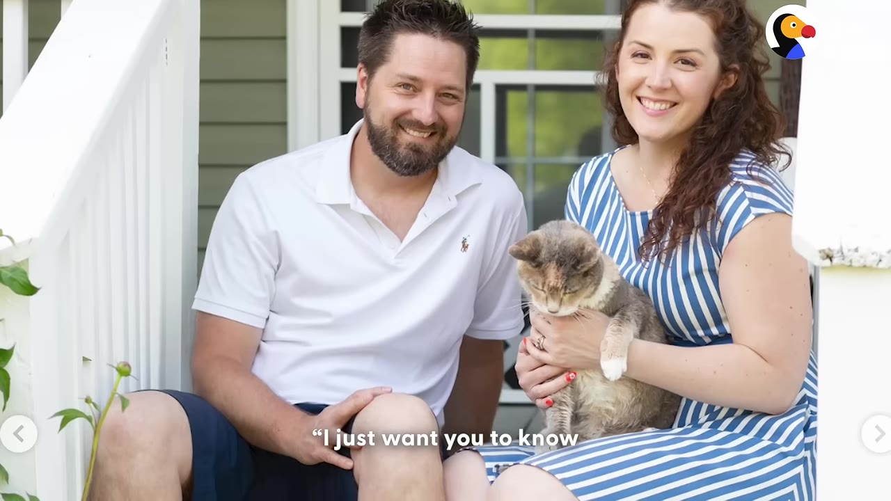 A smiling man and woman sit on porch steps, with the woman holding a grey and white cat in her lap.