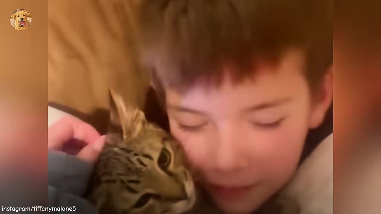 A young boy with brown hair smiles gently as he cuddles a tabby cat close to his face.
