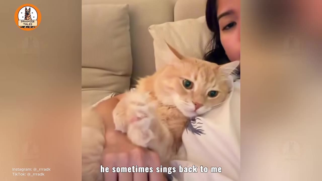 An orange tabby cat lies comfortably on a woman's chest as she holds him, with text on the screen reading 'he sometimes sings back to me'.