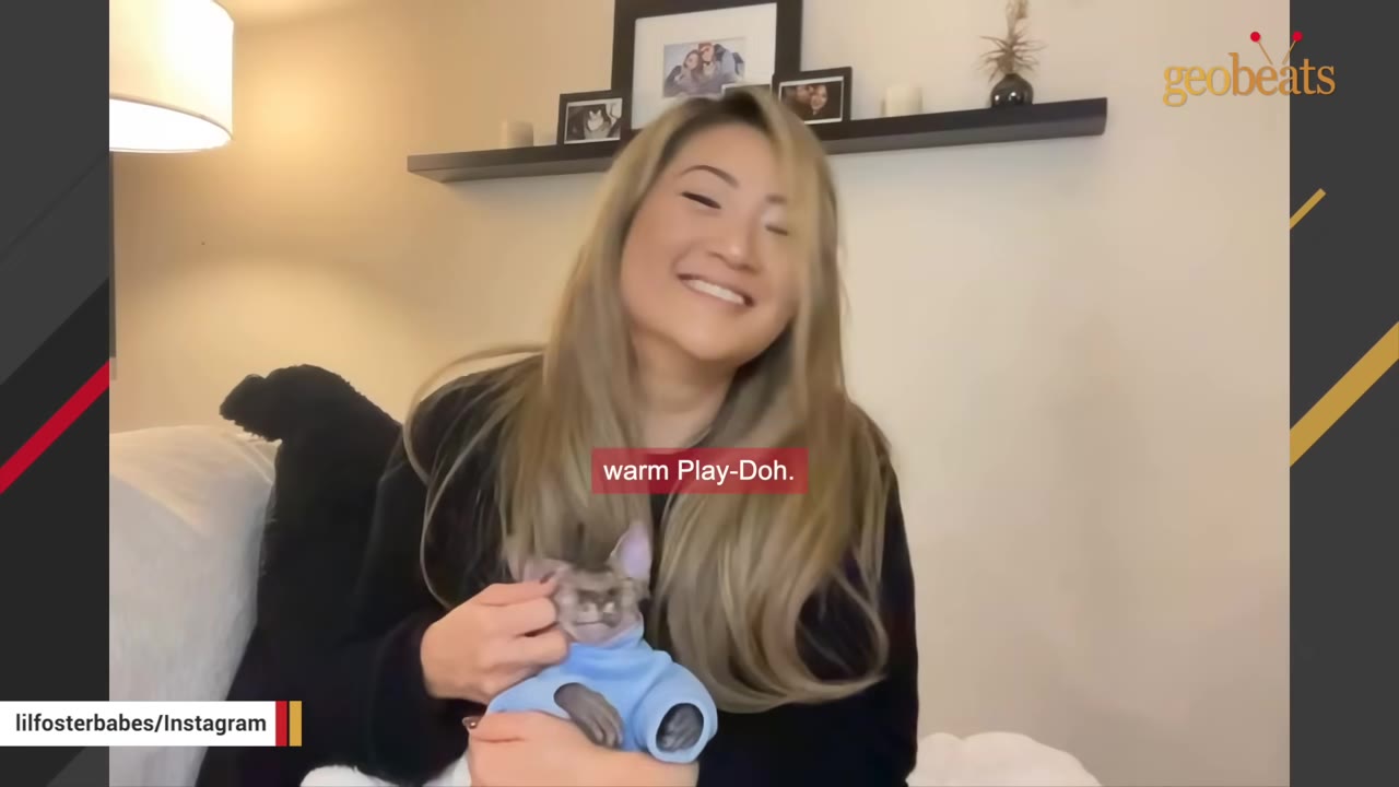 A smiling woman with long blonde hair holds a small Sphynx kitten wearing a blue sweater, with a subtitle reading 'warm Play-Doh.'