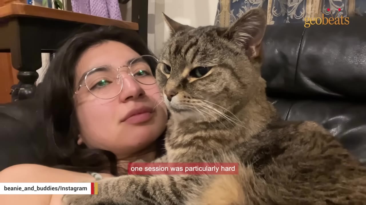 A close-up of Nozomi wearing glasses, lying down with her tabby cat Beanie resting closely against her chest.