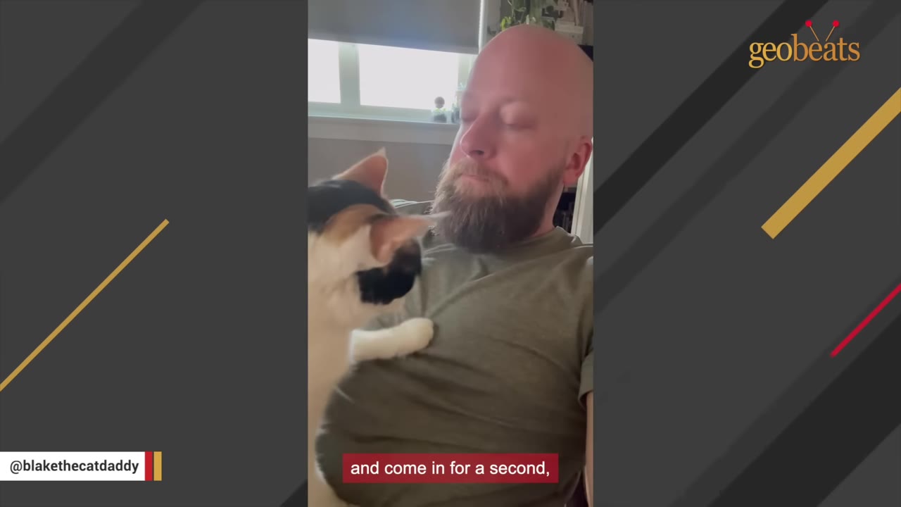 A bearded man with his mouth closed and eyes looking down, holding a calico cat close to his chest.