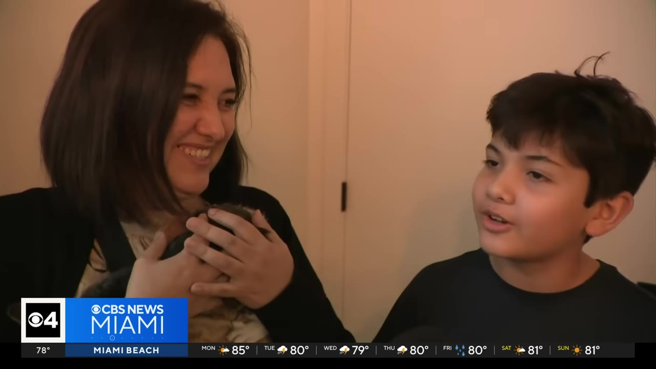 A smiling woman holds a small kitten while a young boy next to her looks on.