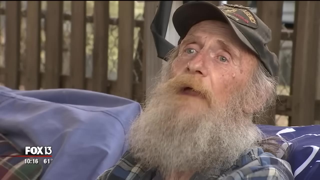 A close-up of an elderly man with a long grey beard and a cap, looking upward with an emotional expression.