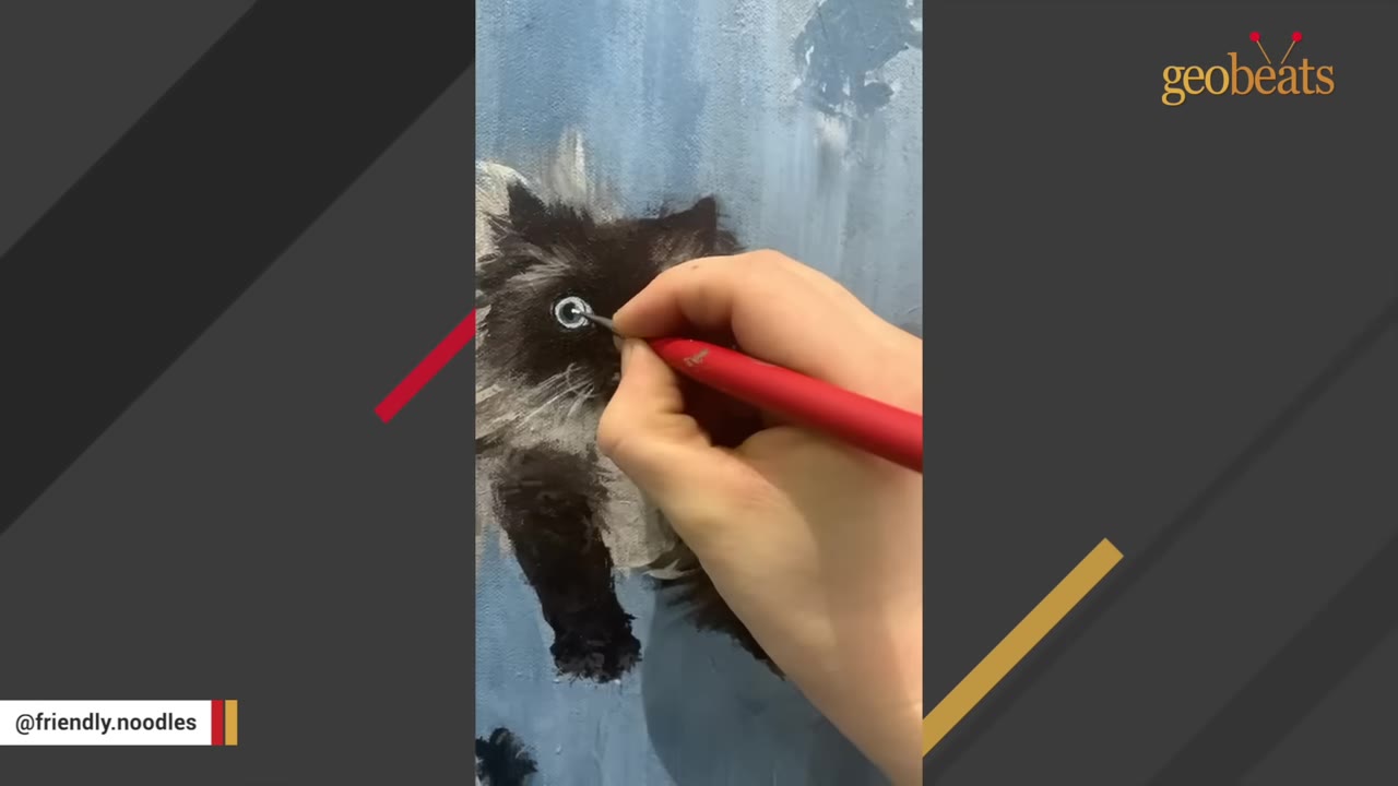 A close-up shot of a hand using a red paintbrush to paint the white highlight of a black cat's eye on a blue canvas.