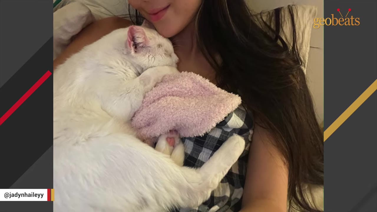 A white cat cuddles closely against a woman's chest while sleeping on a pink blanket.